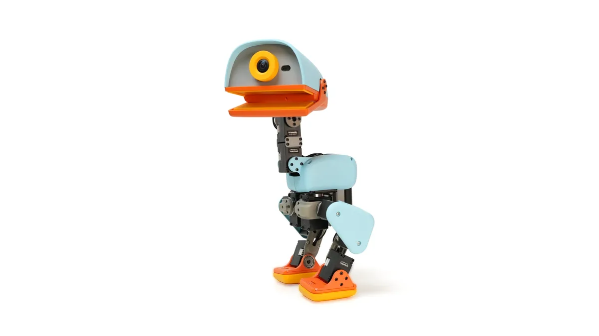 The MicroDuck robot standing on a plain white background, its pale blue head and wide orange beak above black servo-jointed legs with orange feet.